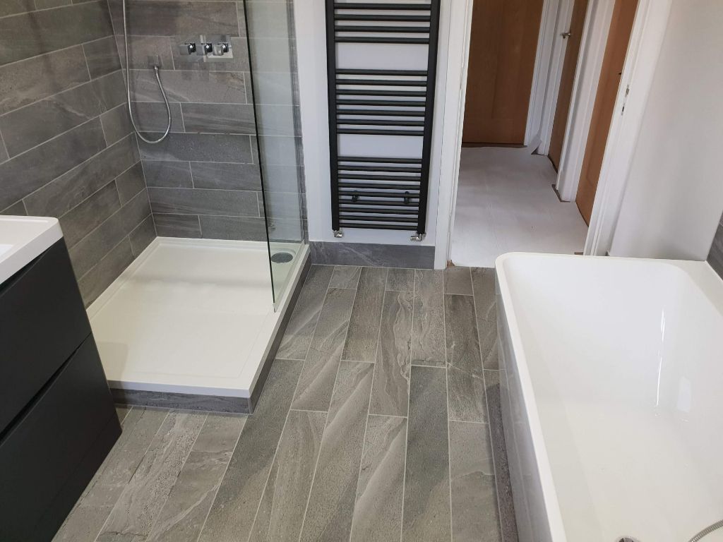 Grey tiled bathroom with walk-in shower and freestanding bath